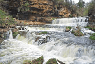 Water cascading over a rocky waterfall in a forested landscape.