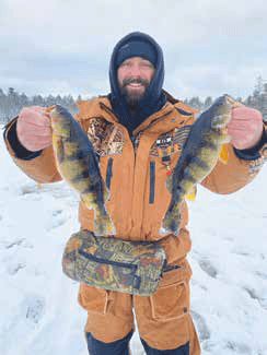 Ice angler holding two yellow perch on a frozen lake.