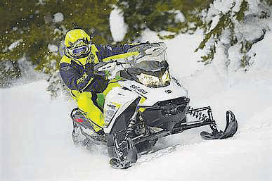 Snowmobiler riding through deep snow in a forested area.