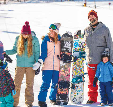 Family standing together at a ski hill with snowboards on a sunny winter day.