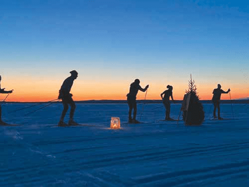 People cross-country skiing on a frozen lake at sunset.