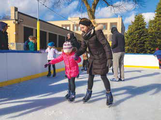 Adult helping a child ice skate at an outdoor rink.