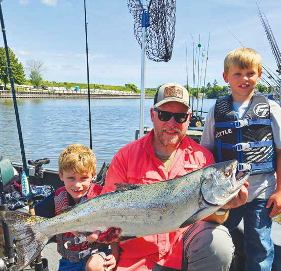 Angler on a boat holding a large salmon with two children.