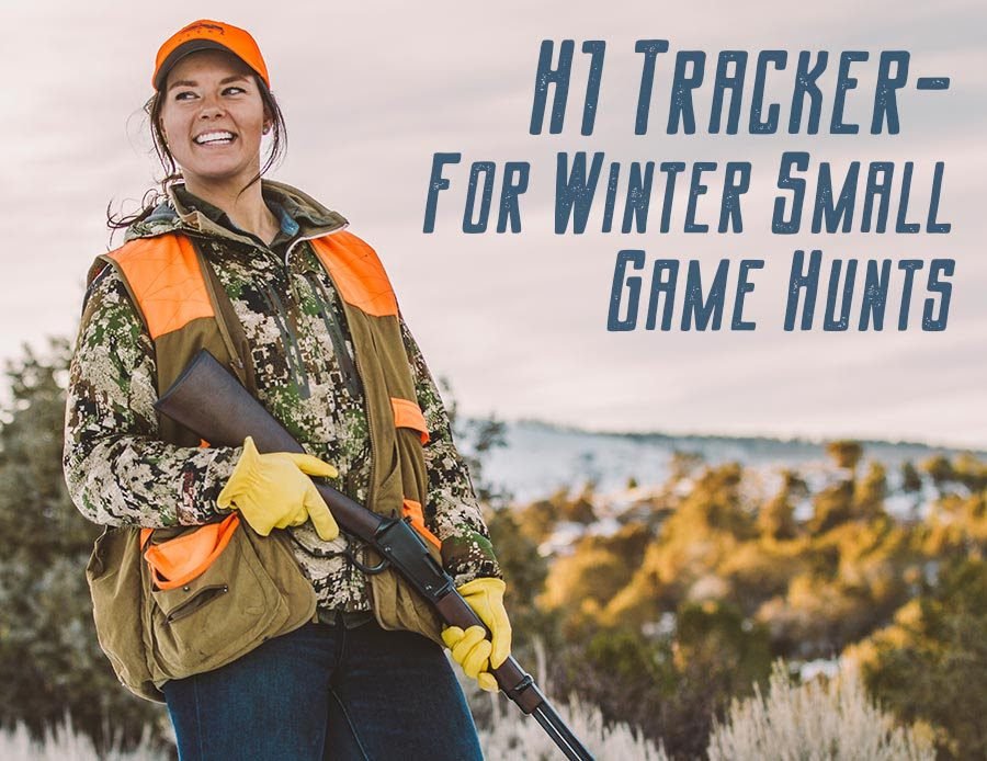 Smiling hunter wearing blaze orange hat and vest with camouflage jacket, holding a lever-action rifle in a snowy, wooded landscape with text reading “H1 Tracker – For Winter Small Game Hunts.”