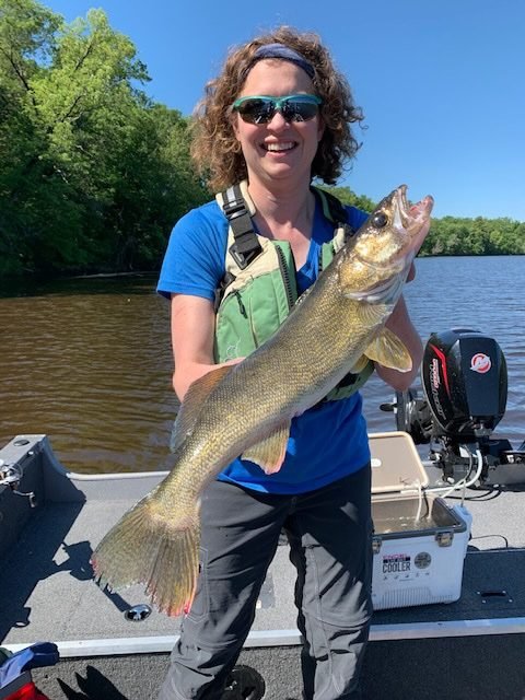 Woman standing in a boat, smiling and holding a walleye